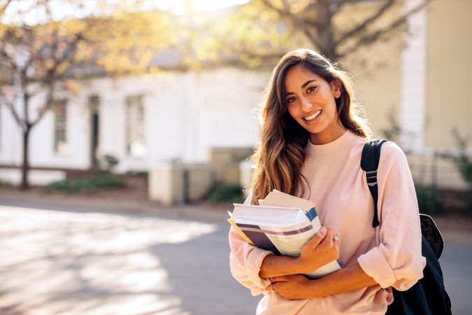 Beautiful female student holding books while standing on college campus