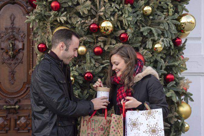 Happy young couple with paper bags standing near Christmas tree