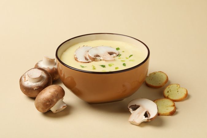 Mushrooms surrounding bowl of soup on beige background