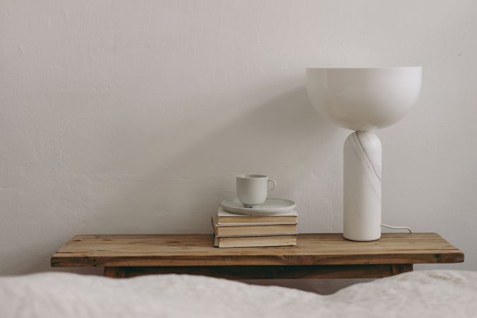 Cup of coffee, books and modern marble geometric lamp on vintage teak wooden bench