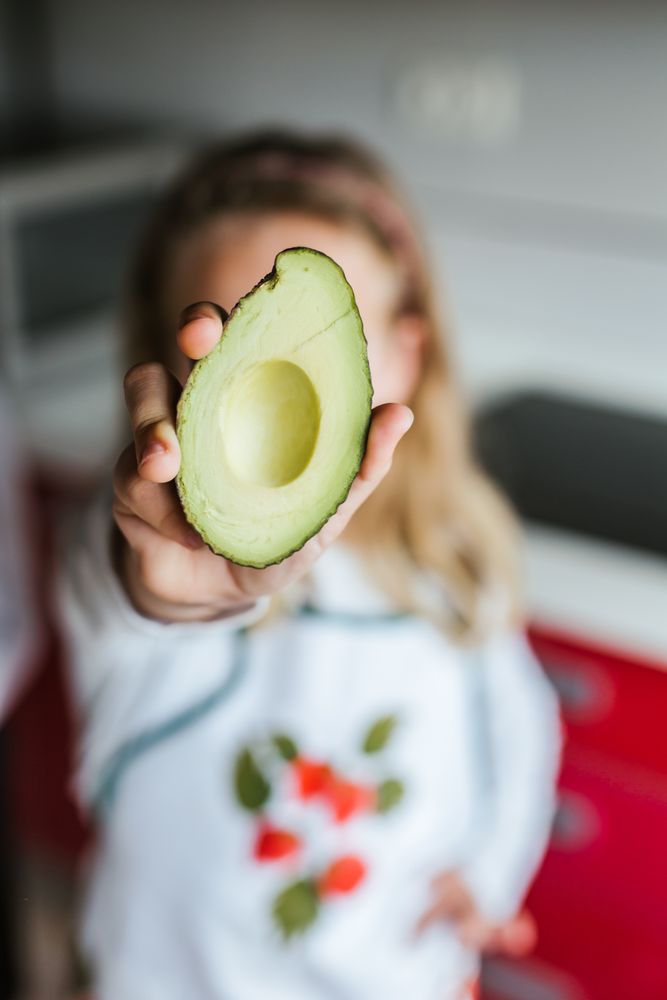 Crop kid showing cut avocado
