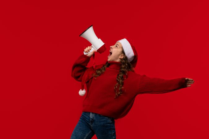 Excited girl in Santa hat and sweater shouts into megaphone