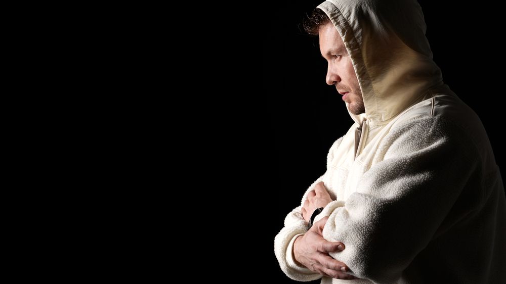 Man wearing hooded fleece jacket, arms crossed, side profile.