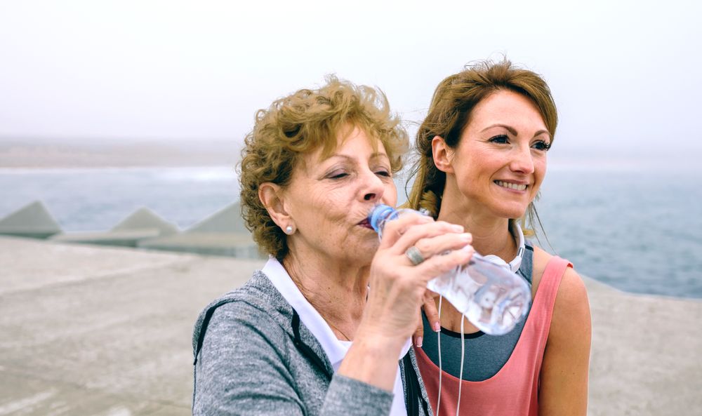 Older sportswoman drinking water with female coach