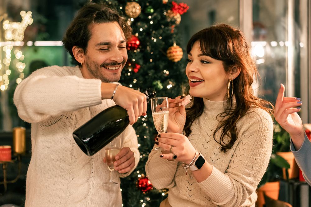 Happy young couple celebrating Christmas by pouring champagne together.