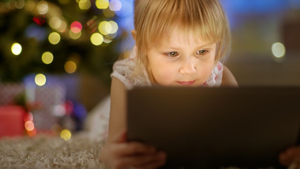 Little Girl With Tablet Computer in Her Hands Lies on the Carpet under the Christmas Tree.