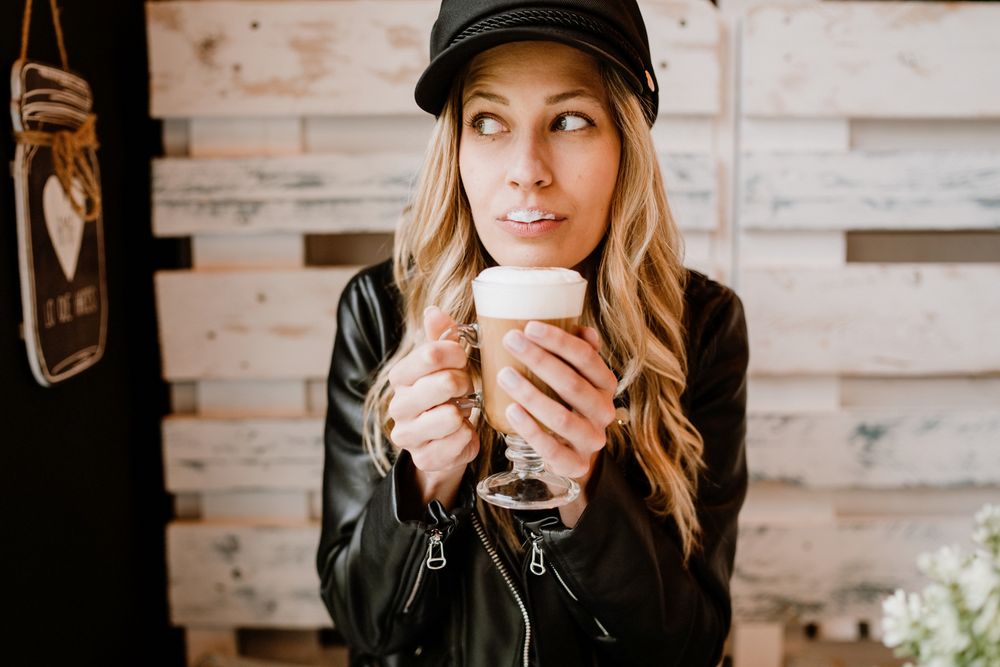 Stylish woman holding coffee in hands and licking lips