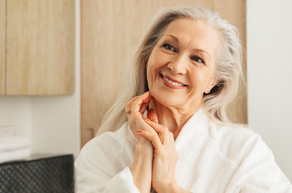 Smiling female in bathrobe looking in mirror with hands on chin