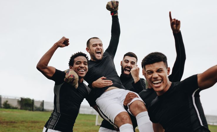 Group of happy soccer players celebrating a win by lifting their goalkeeper