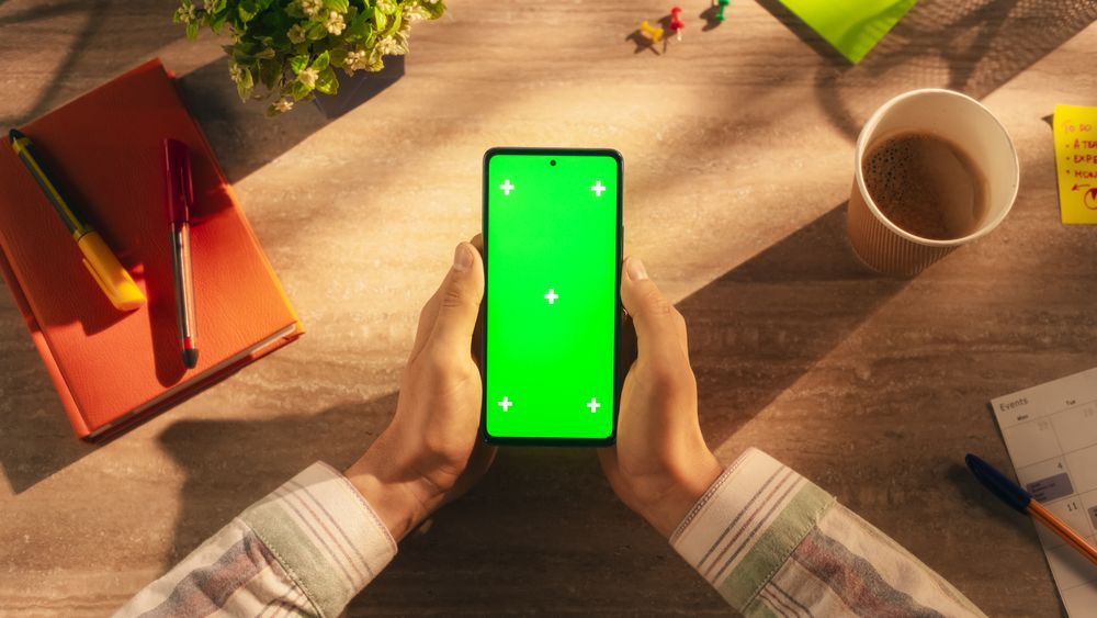 Office Worker Holding a Modern Mobile Phone in Front of a Camera. Smartphone with Green Screen Chroma Key Template for Digital Marketing, Promotion of Online Services, App, Software, Media Campaigns