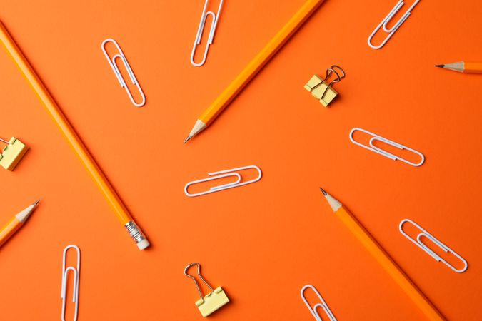 Pencils and paper clips on orange background