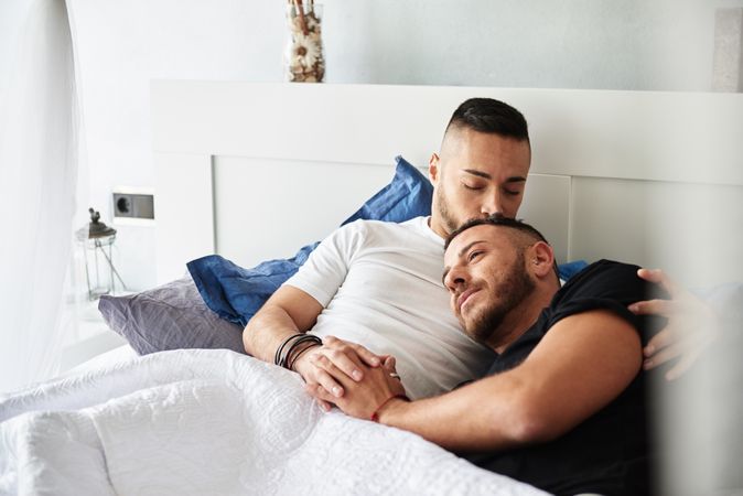 Smiling gay couple hugging and kissing on bed