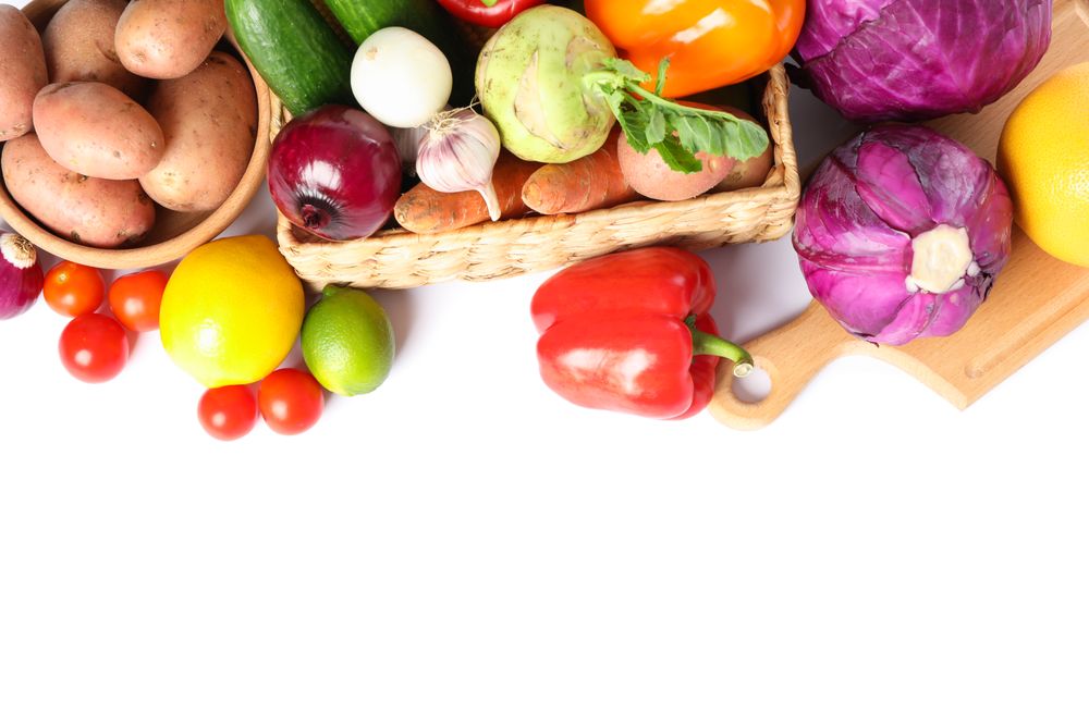 Wicker basket, wood board and vegetables isolated on plain background