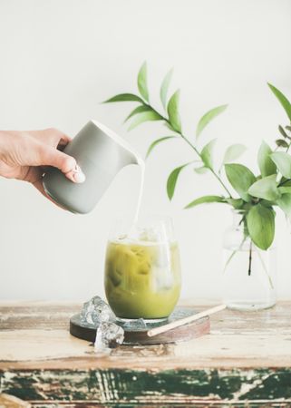 Iced matcha drink with hand pouring cream