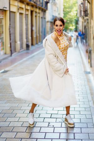 Happy fashionable woman standing in street with long coat and geometric dress