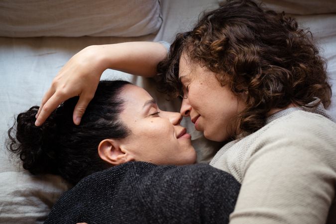 Two women lying down and embracing with noses touching