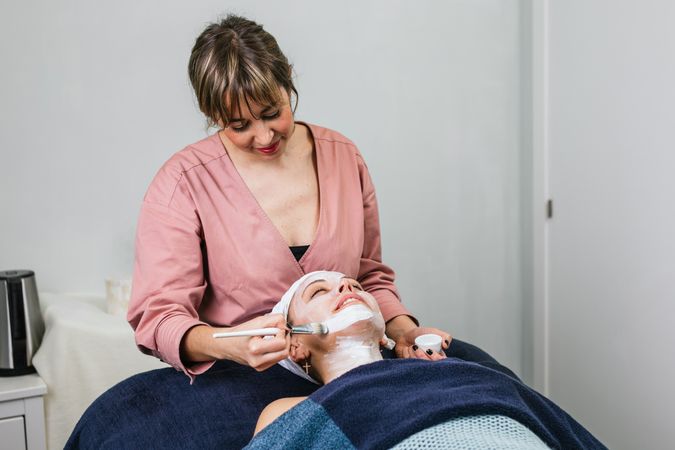 Professional beautician applying facial mask on face of client
