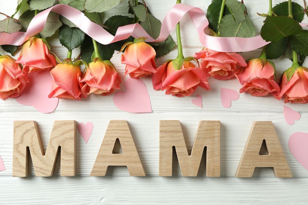 Inscription Mama with pink roses, ribbon and little hearts on wooden background, top view
