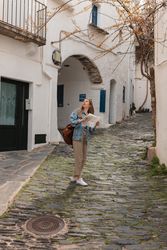 Woman standing in middle of narrow town street holding map and looking up