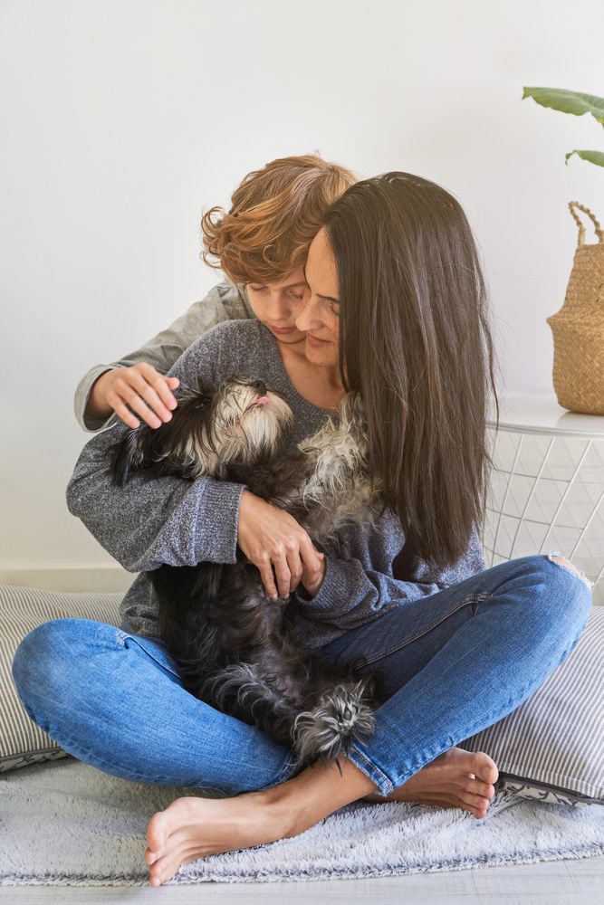 Mother and son hugging dog together at home