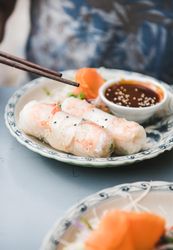 Chopsticks held above spring rolls, with dipping sauce