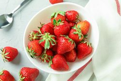 Plate with fresh strawberries, spoon and kitchen towel on bright background, top view and space for text