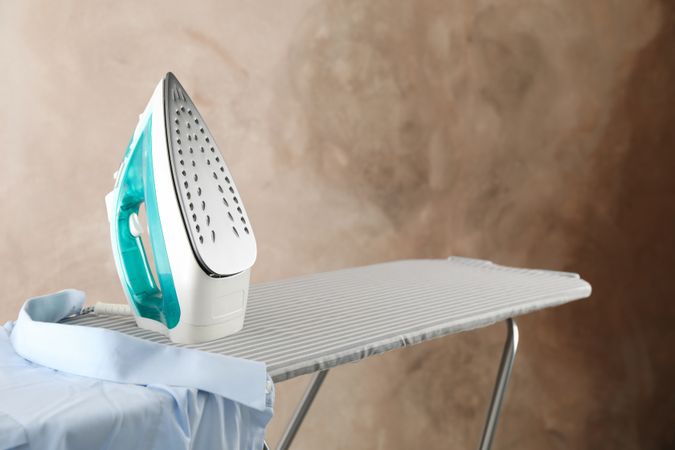 Iron and shirt on ironing board against brown background, space for text
