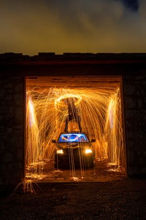 Person with burning round on car in garage in darkness