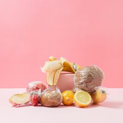 Plastic wrapped fruit on pink background