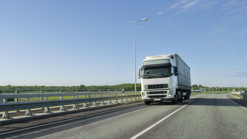 Big Semi Truck with Cargo Trailer Drives on the Industrial Area Empty Road With Sun Shining in the Background.