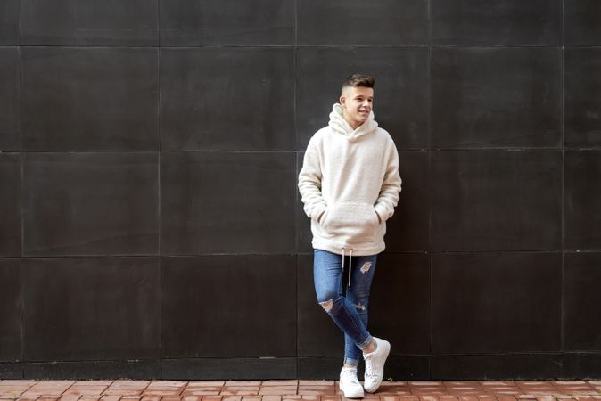 Young man in bright hoodie leaning on dark wall outside, vertical composition with copy space
