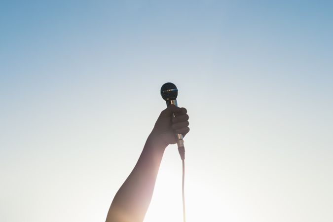 man hand holding a microphone outdoors with sunlight reflects