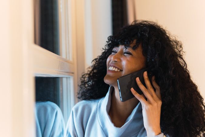Cheerful Black woman talking smartphone at home