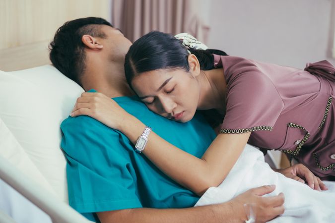 Concerned wife hugging husband in hospital bed