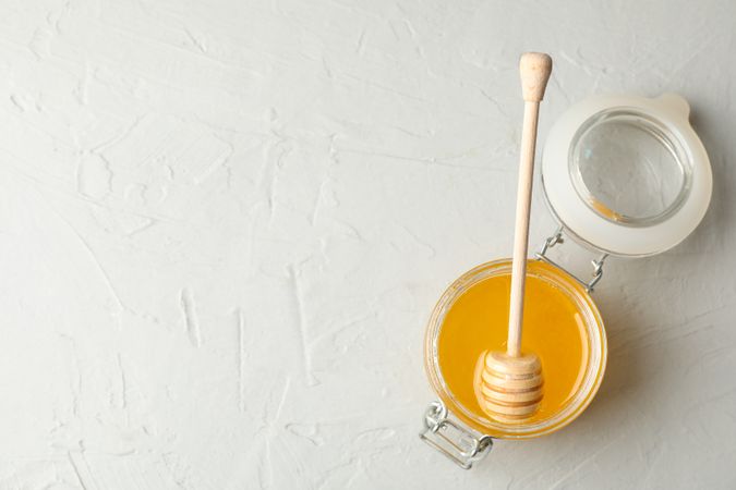 Glass jar with honey and dipper on neutral background, top view