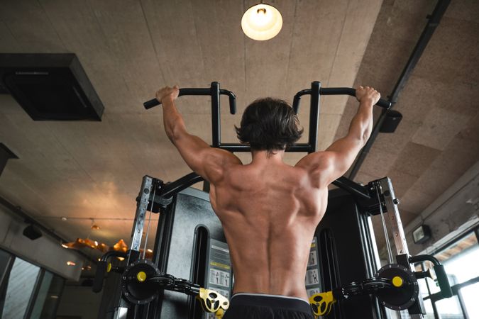Muscular guy doing pull ups on exercise machine