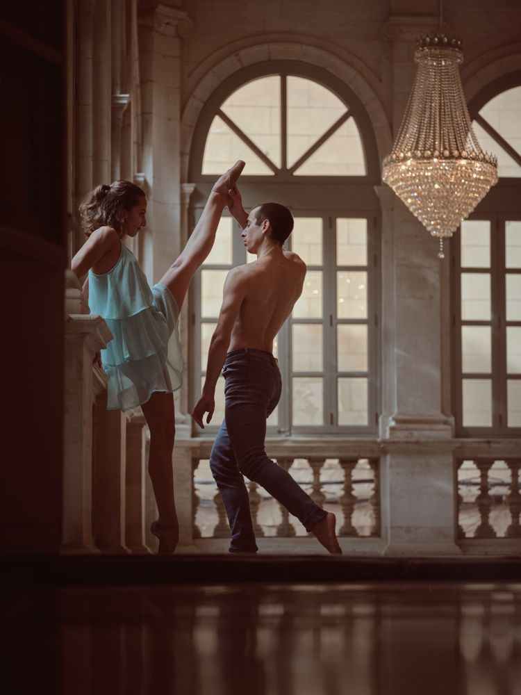 Ballet dancer raising leg of female partner in hall
