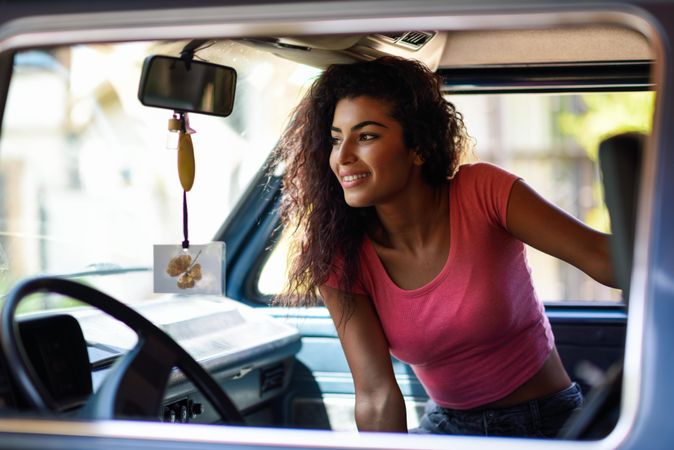 Female in pink t-shirt with curly hair sitting up in passenger side of car