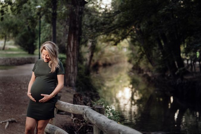 Happy pregnant woman standing at river in park