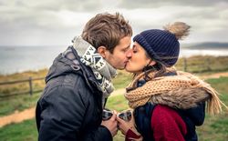Man and woman kissing while holding warm beverage on cold day