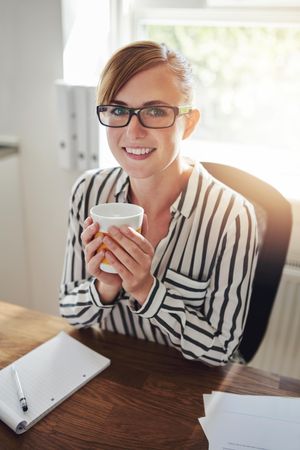 Content female in striped shirt with coffee at her desk