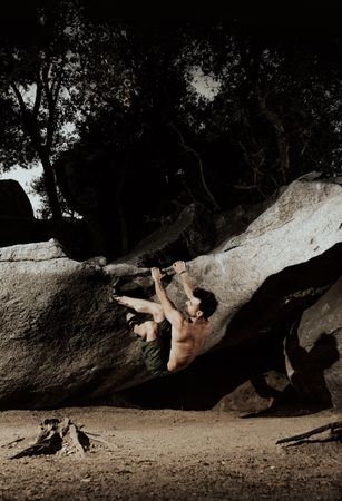 Man practicing rock climbing among large rocks in a forest
