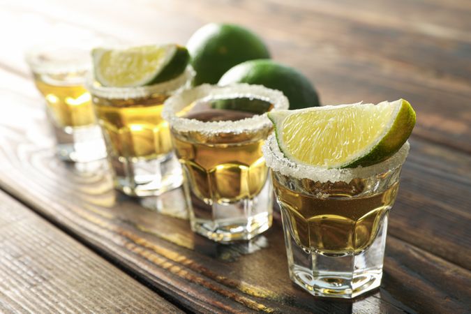 Tequila shots with salt and lime slices on wood table, closeup