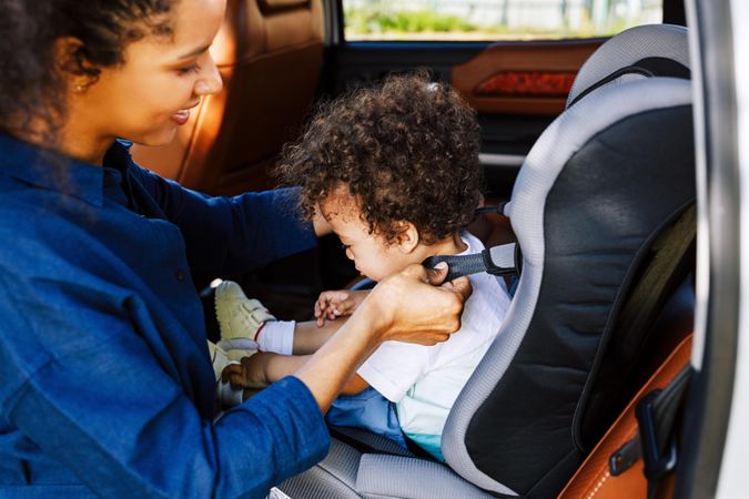 Little boy being secured by mother in car seat