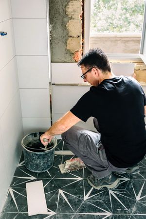 Mason taking cement from bucket to lay bathroom tiles