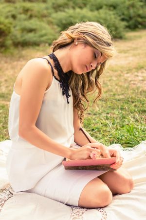 Romantic woman writing in a diary sitting outdoors