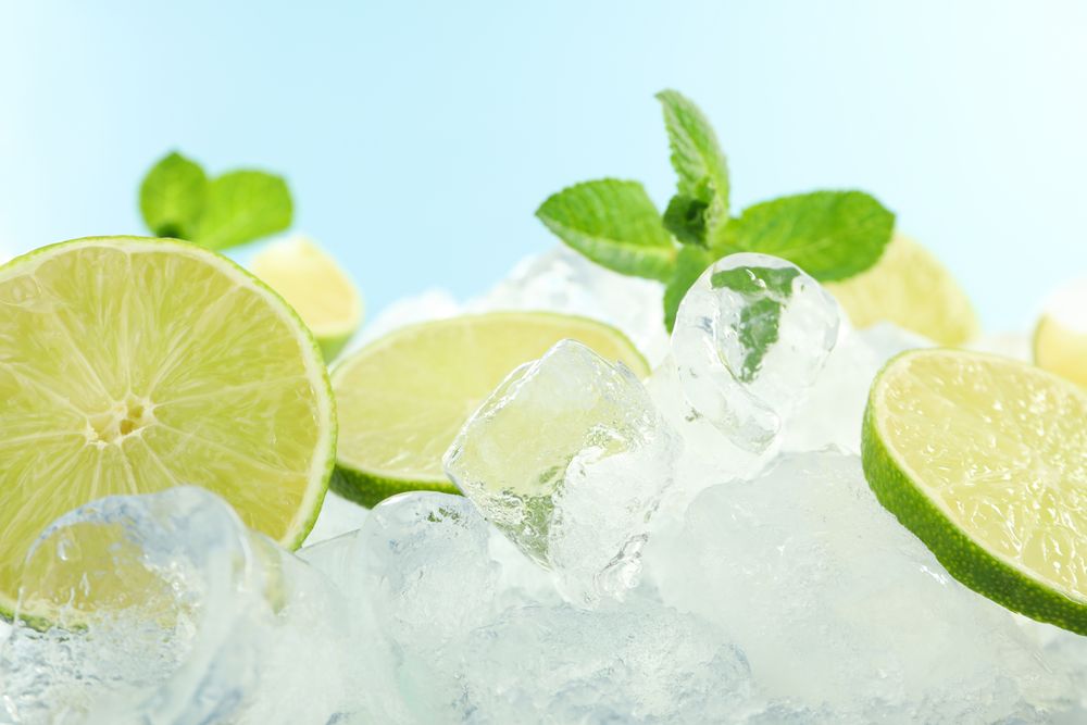 Pile of ice with lime halves and mint in blue room, copy space