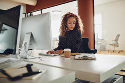 Woman with curly hair checking her notes at computer at work