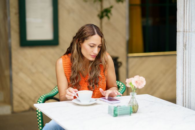 Woman enjoying morning coffee using phone in a pavement cafe