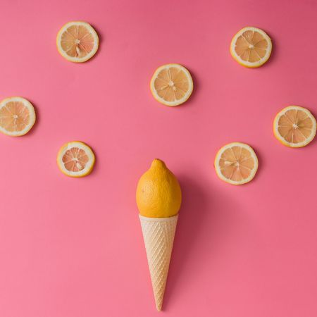 Lemon fruit in ice cream cone with lemon slices on pink background